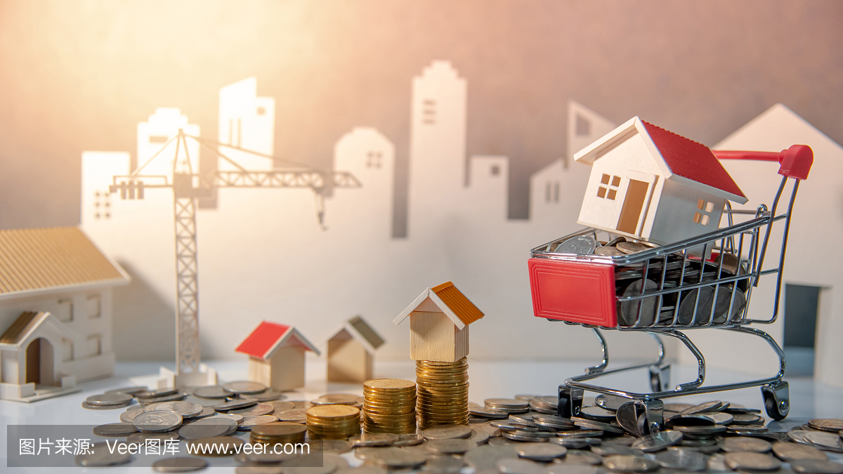 房地产或房地产投资概念。住房抵押贷款利率。建筑业投资。房子模型和硬币在迷你购物车(手推车)在桌子上与起重机和城市背景。